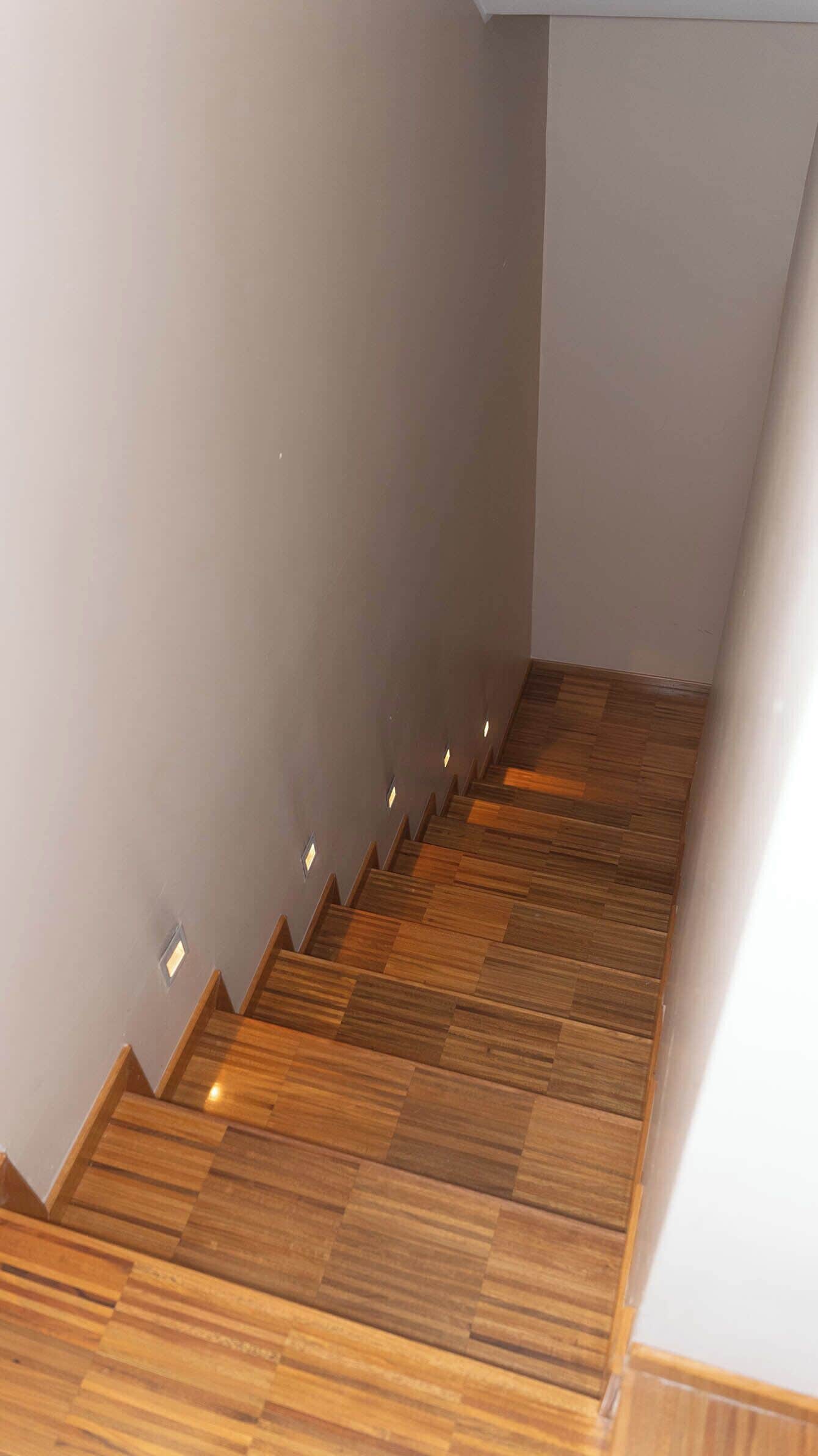 Una scala in legno dal design moderno, con una parete chiara e un pavimento in legno.