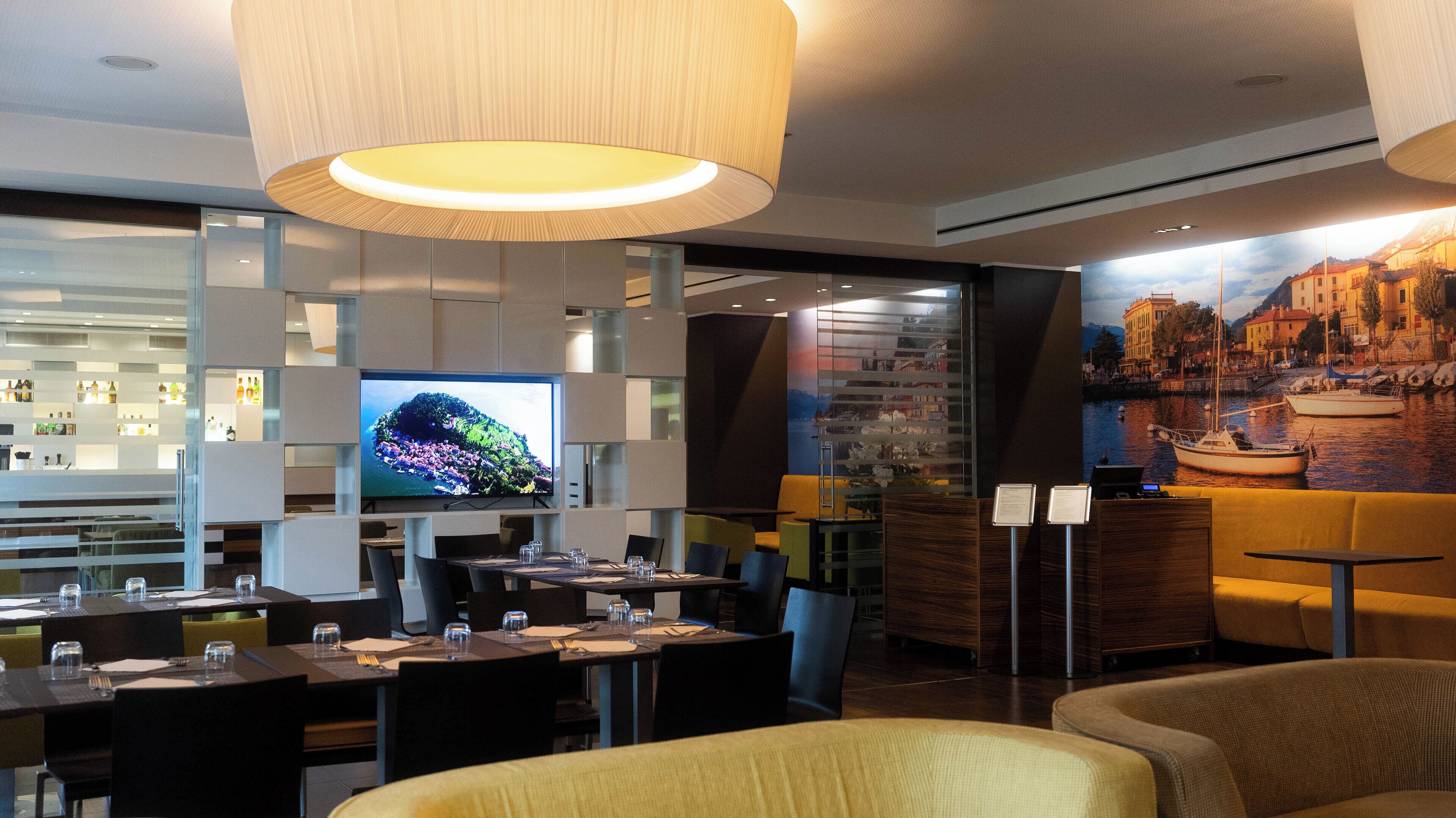 En modern restaurang med en stor TV-skärm, trämöbler och en väggmålning som föreställer ett kustlandskap.