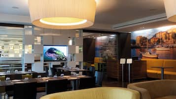 A modern restaurant with a large TV screen, wooden furniture, and a mural of a coastal scene.