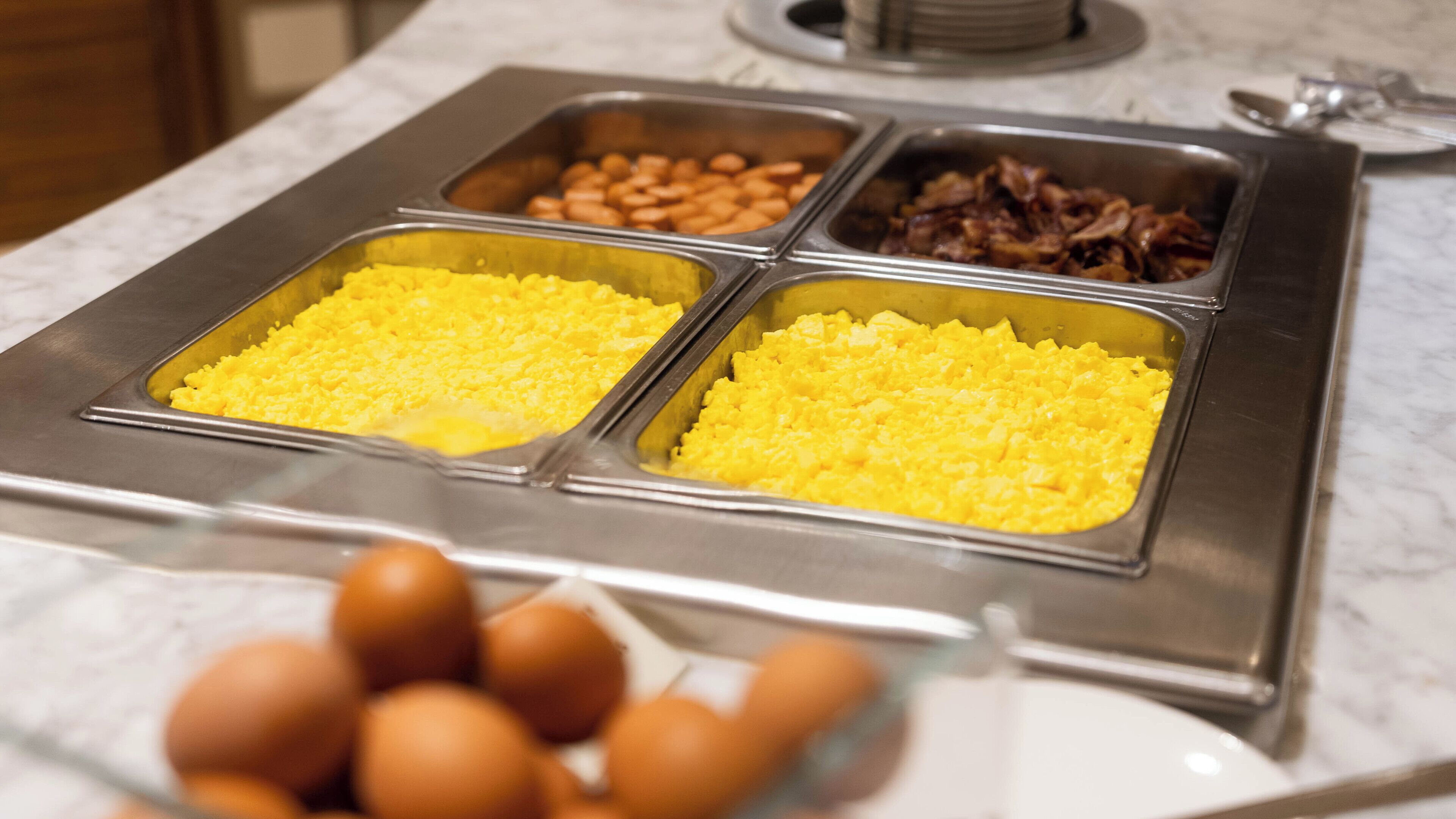 A buffet with scrambled eggs, beans, and bacon.
