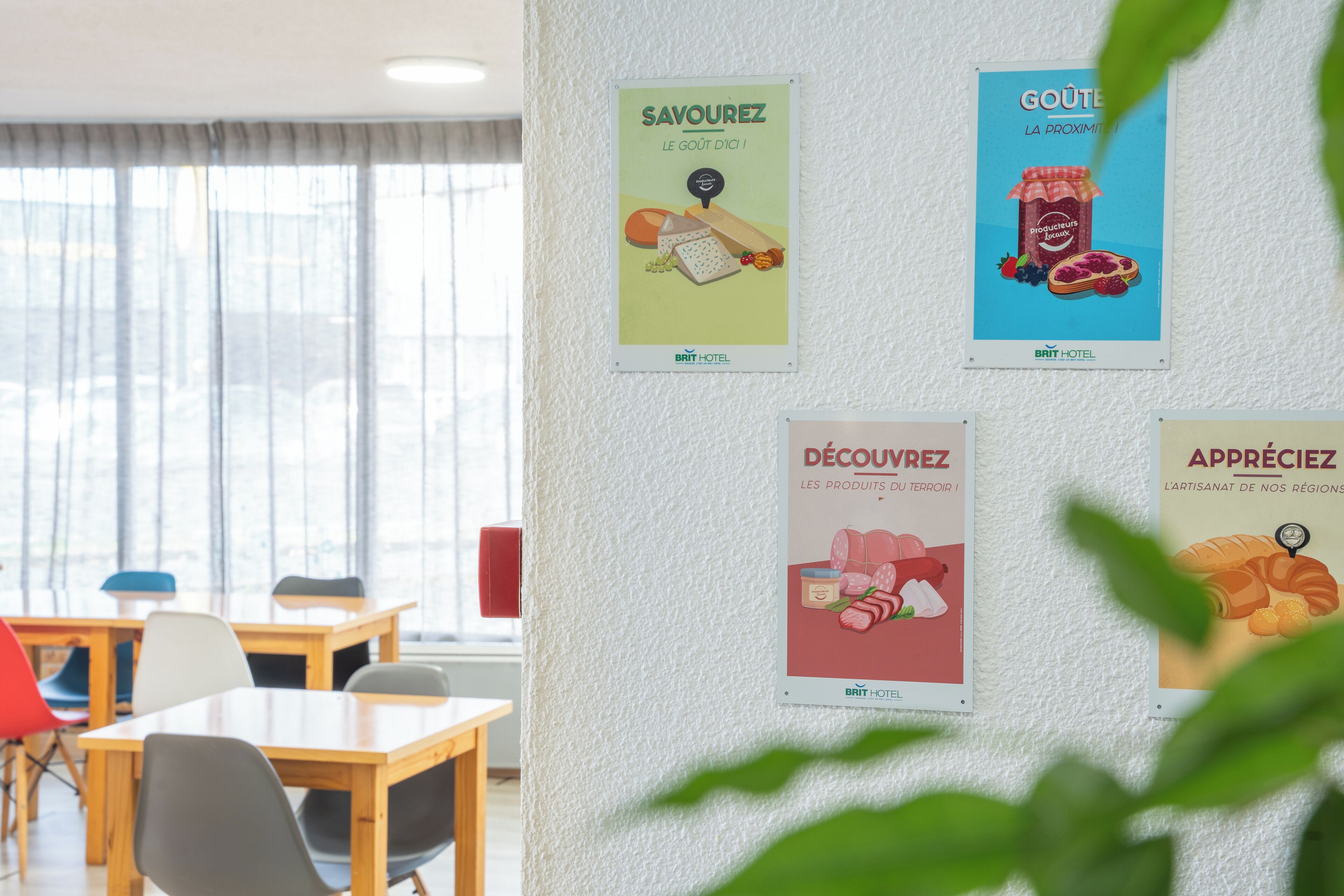 A hotel room with a large window, a wooden table, and four posters on the wall promoting local products.