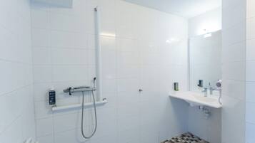 A small, modern bathroom with white tiles, a shower, a sink, and a mirror.
