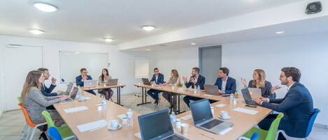 A conference room with a long table, laptops, and people engaged in discussion.
