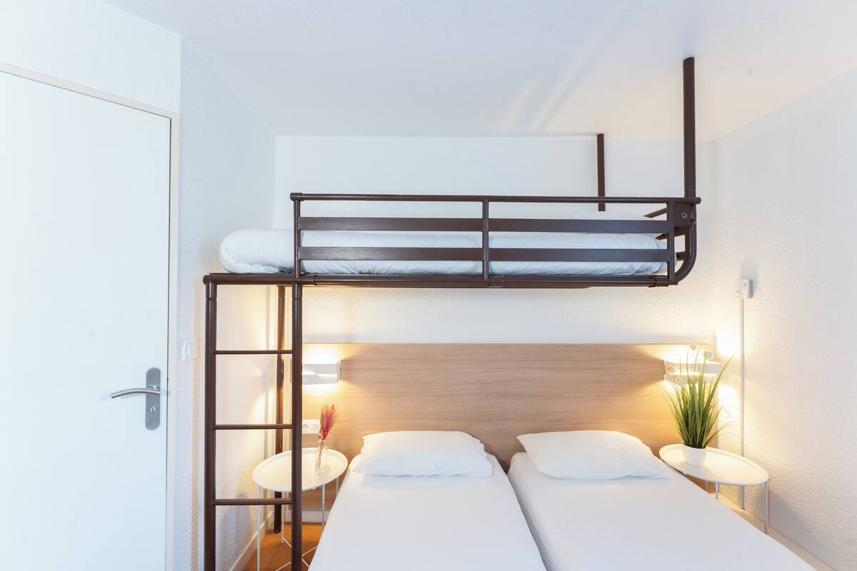 A bunk bed with a ladder, two bedside tables with lamps, and a potted plant.