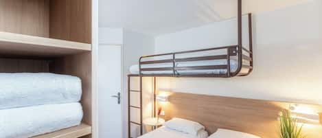 Una habitación con literas, un cabecero de madera, una mesita de noche con una lámpara y una toalla en el estante.