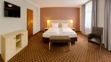 A hotel room with a double bed, two bedside tables with lamps, a wooden cabinet, a chair, and a TV mounted on the wall.