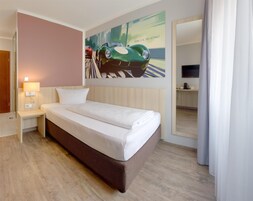 A hotel room with a bed, a nightstand, a lamp, a painting of a car on the wall, and a mirror.
