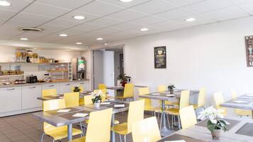 A dining area with yellow chairs and tables, a kitchen area with various food items and appliances, and a wall with a framed sign.