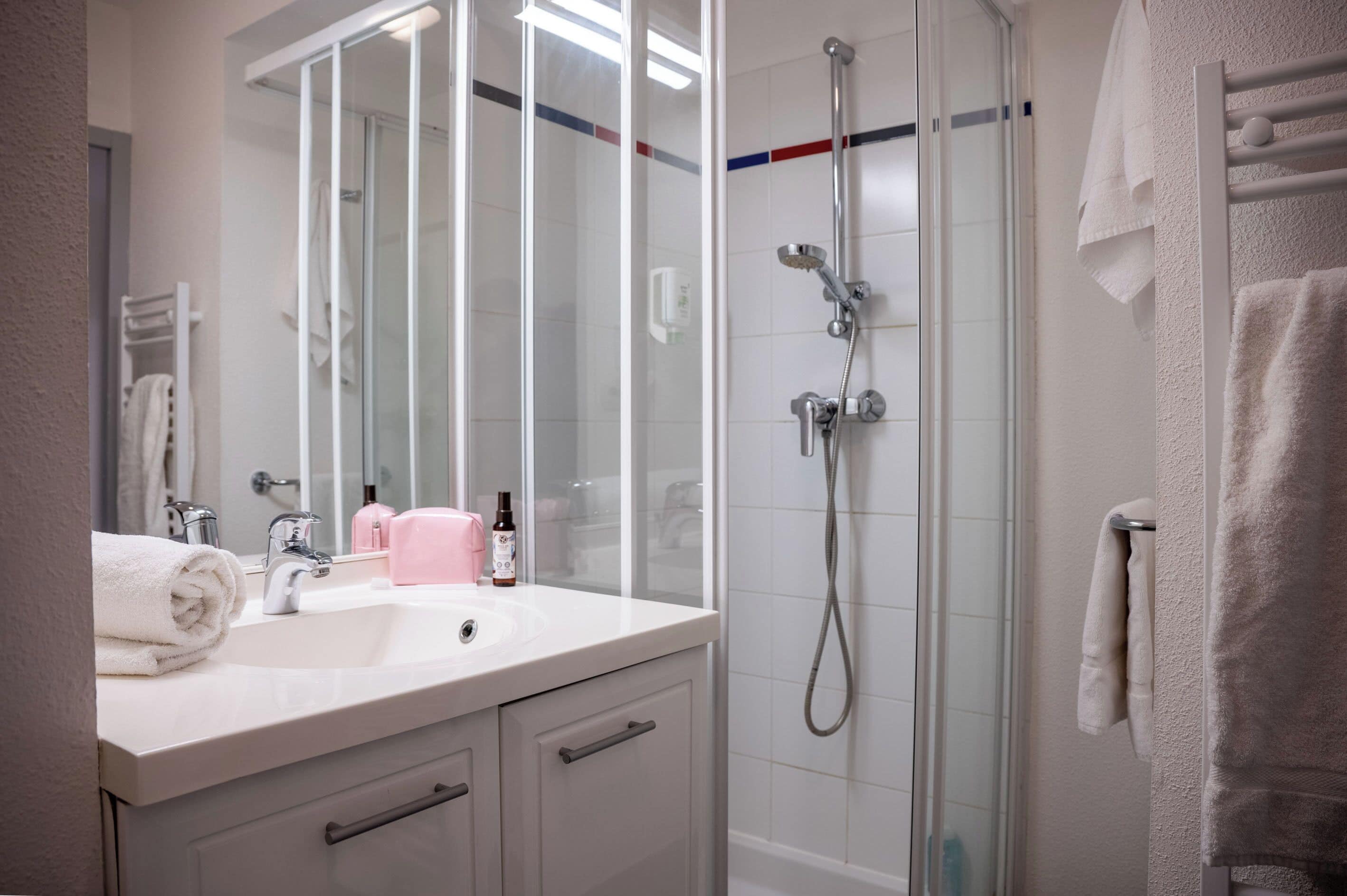 Une salle de bain avec une douche à parois de verre, un lavabo blanc et un miroir.