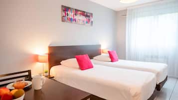 Ein Hotelzimmer mit zwei Betten, einem Nachttisch mit Lampe, einer Obstschale und einem Bild an der Wand.