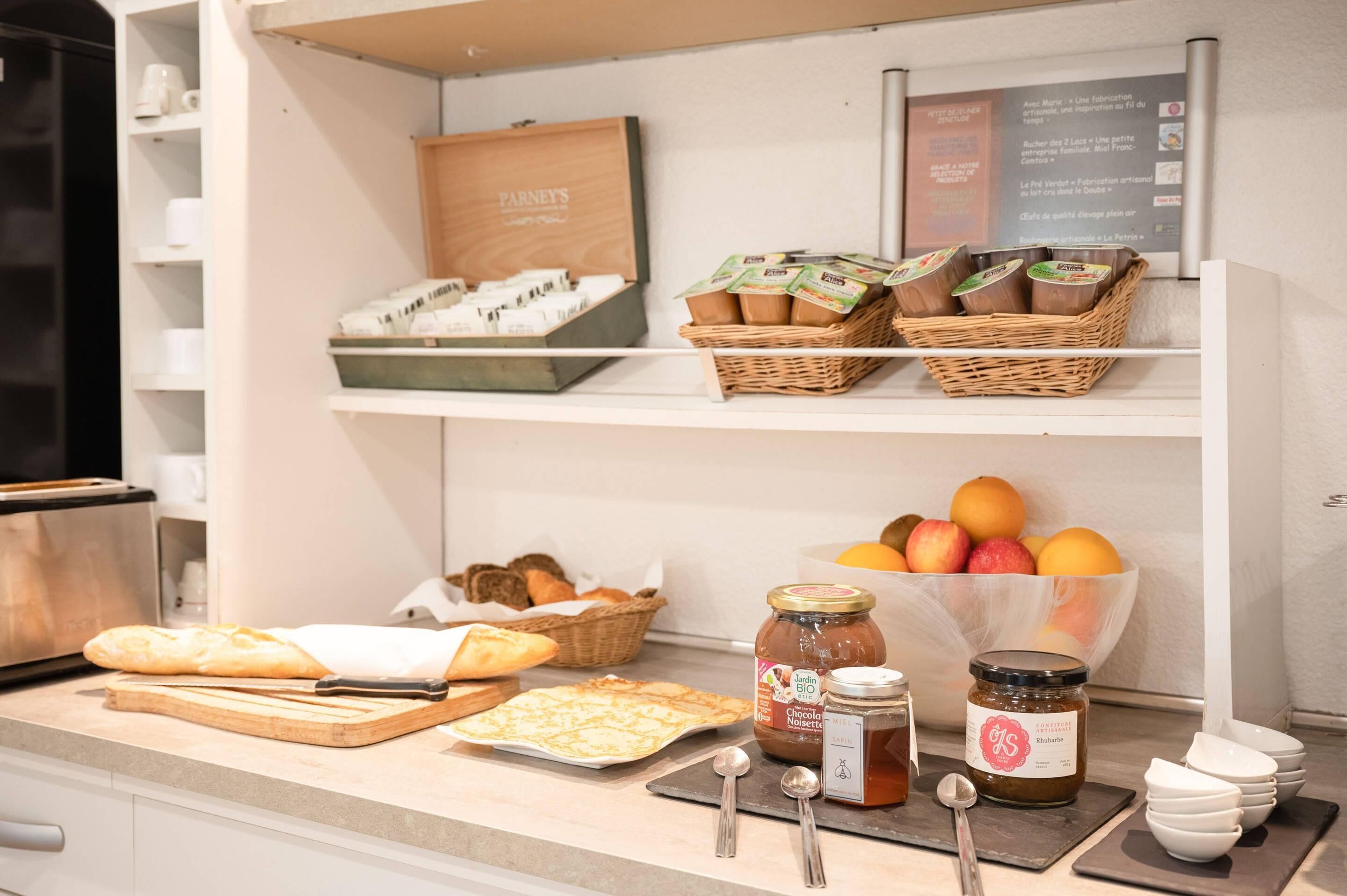 Una encimera de cocina con pan, pasteles, frascos de conservas y una cesta de frutas.