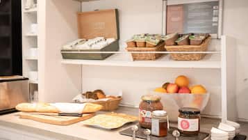 Una encimera de cocina con pan, pasteles, frascos de conservas y una cesta de frutas.