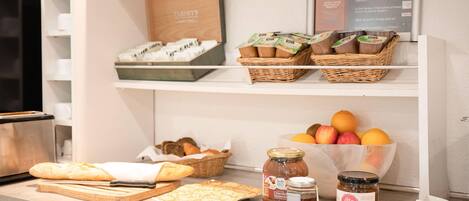Una encimera de cocina con pan, pasteles, frascos de conservas y una cesta de frutas.