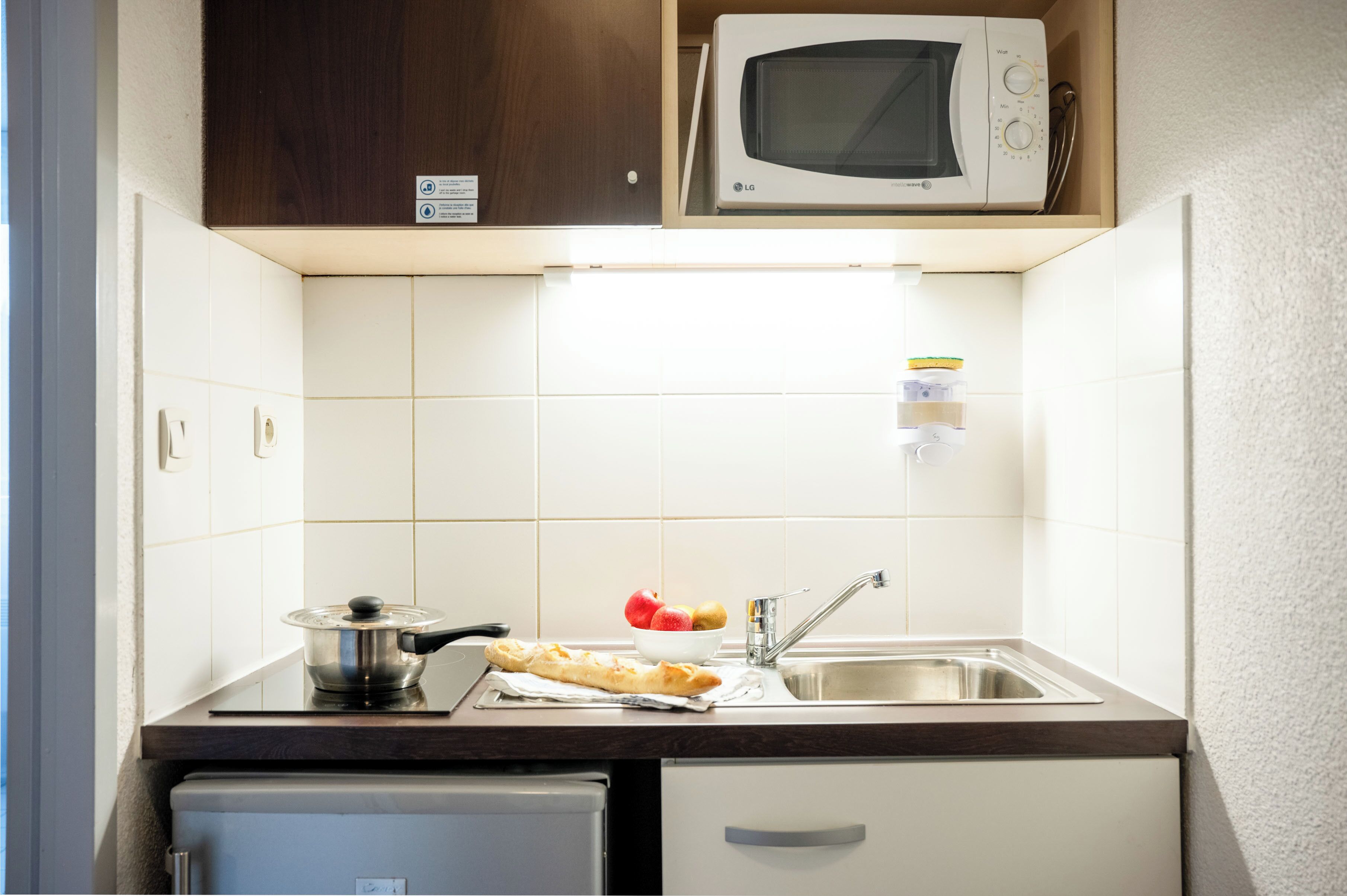 Pieni, käytännöllinen keittiö, jossa on mikroaaltouuni, pesuallas ja pieni jääkaappi.