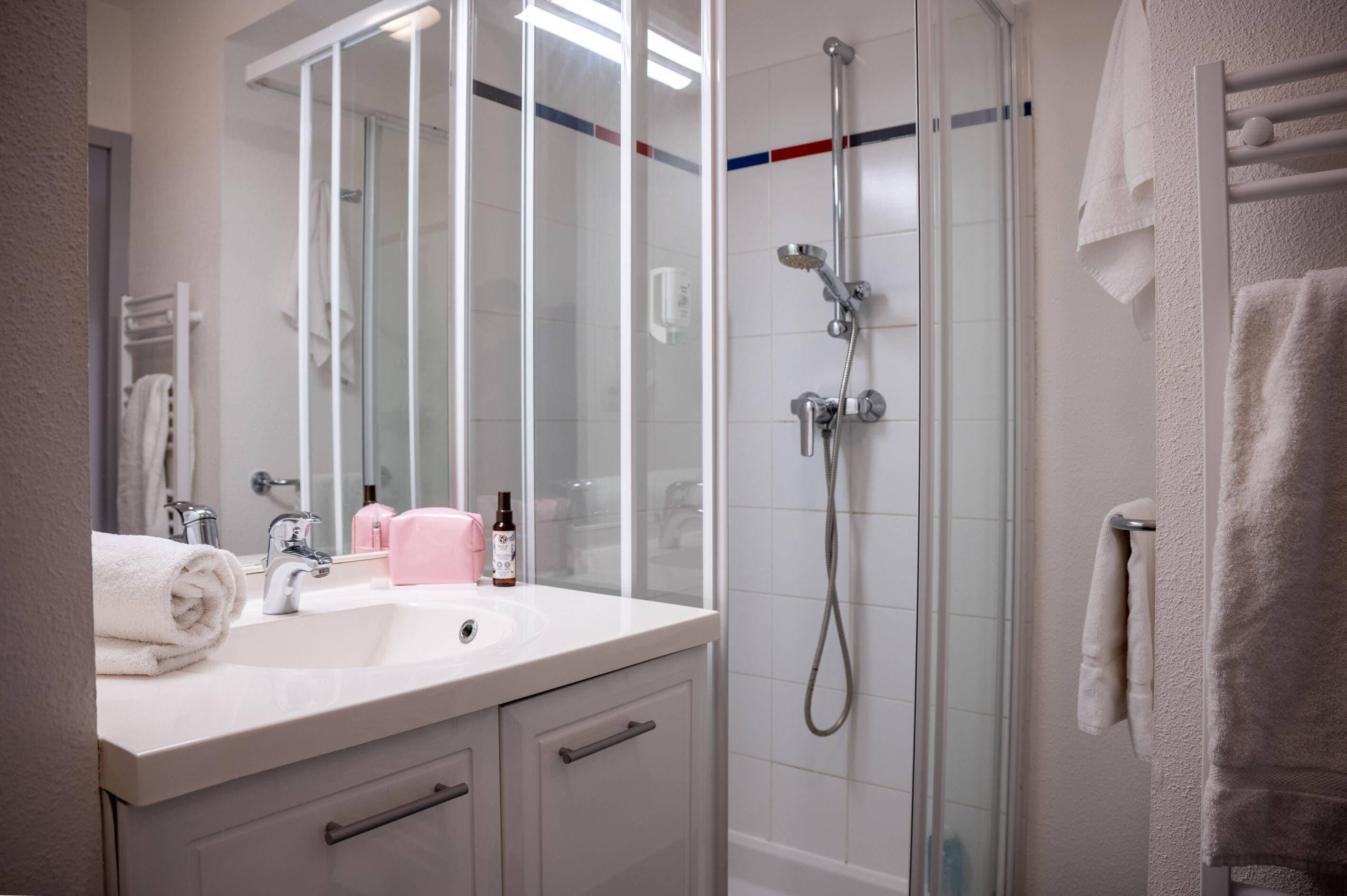 A modern bathroom with a glass shower enclosure, a white sink with a mirror, and a towel rack.