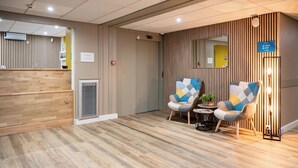 A reception area with a wooden reception desk, two patterned armchairs, a small table with a plant, and a mirror on the wall. - Comfort Aparthotel Besancon La City (Besancon)