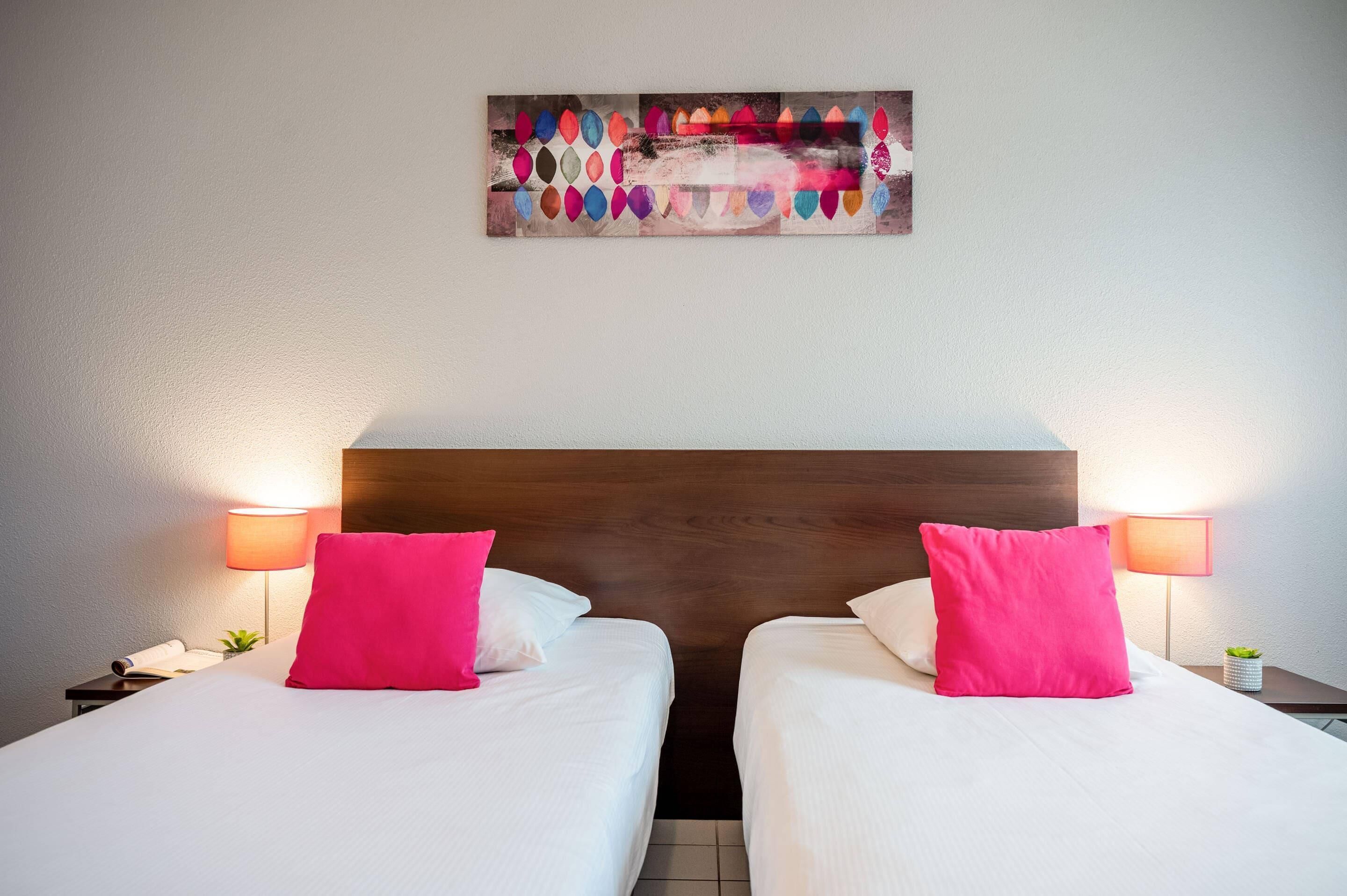 A hotel room with two beds, a wooden headboard, bedside lamps, and a wall art piece.