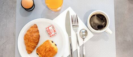 A breakfast setting with croissants, a glass of orange juice, a cup of coffee, and a plate with a biscuit.