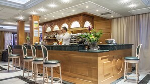A bar area with a wooden counter, bar stools, and a bartender. - Grand Hotel Bonanno (Pisa)