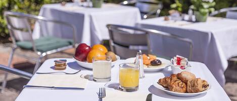 Mobiliario de comedor al aire libre con mesas, sillas y una variedad de comida y bebidas.
