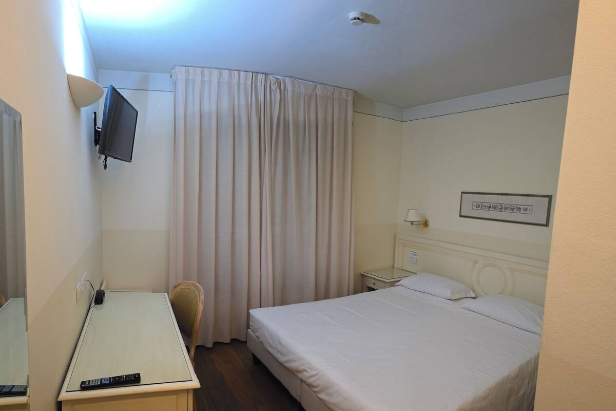 A hotel room with a bed, a desk, a chair, a TV, and a bedside table.