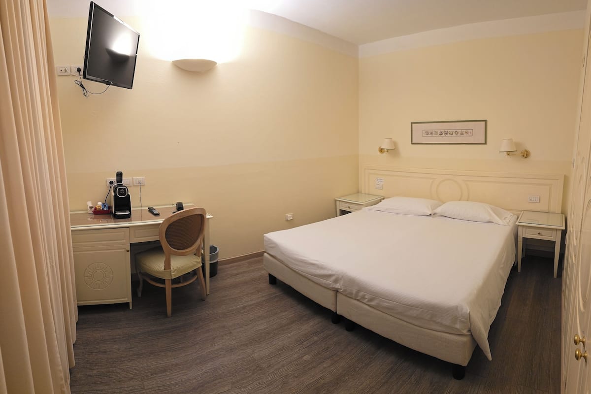 A hotel room with a bed, desk, chair, and a TV mounted on the wall.