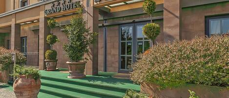 El exterior del Grand Hotel Bonanno, con escalones que conducen a la entrada, grandes macetas con plantas y una vista despejada de las puertas.