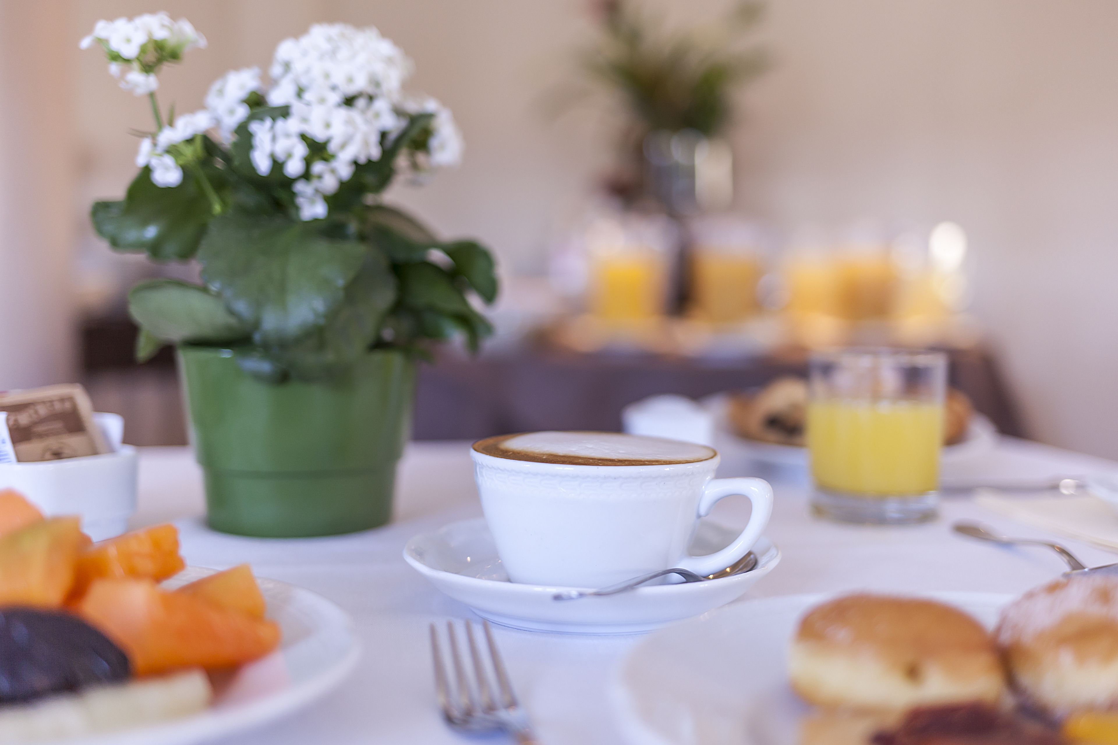 A breakfast setting with a cup of coffee, a plate of fruit, pastries, and a glass of orange juice.