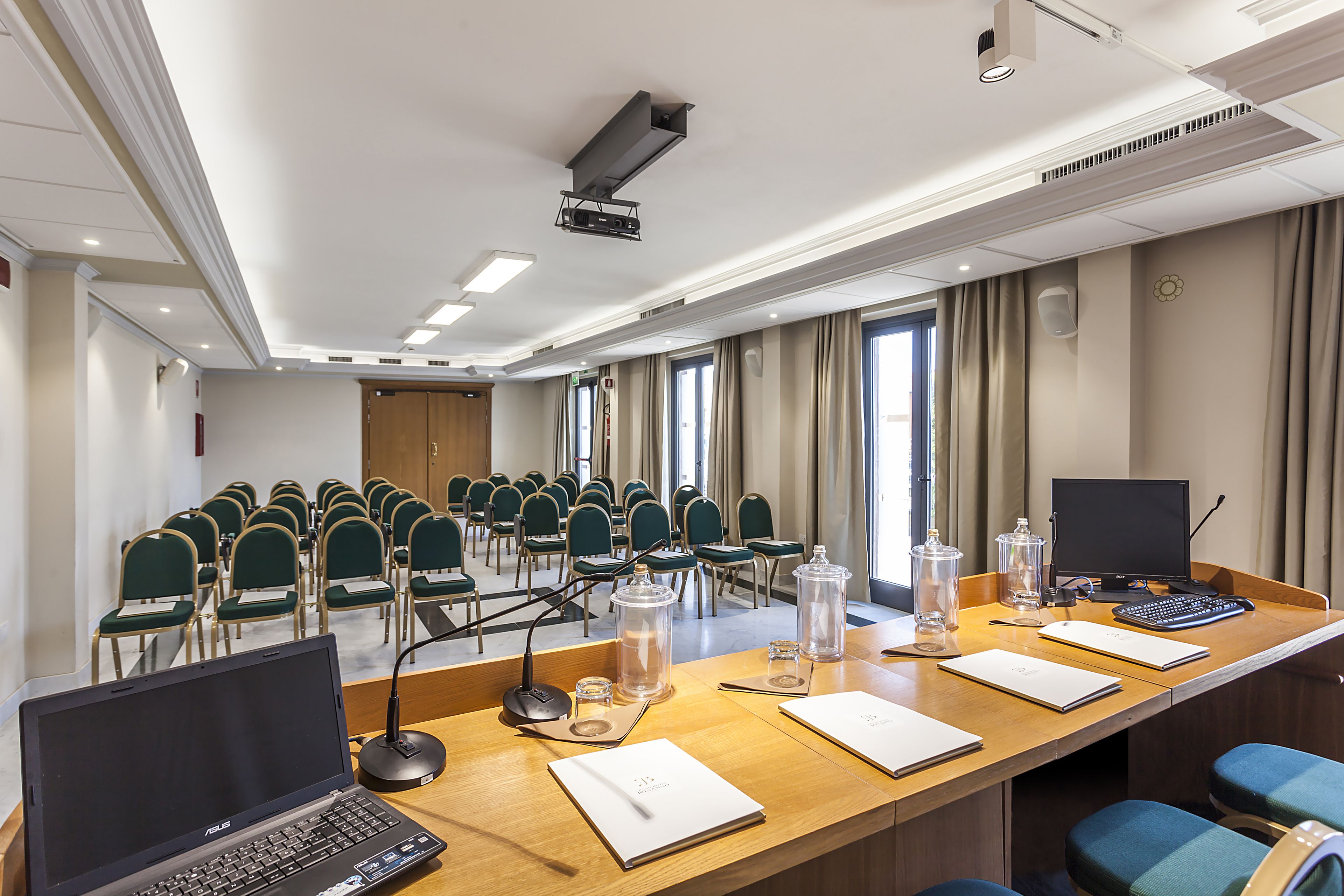 A conference room with a long table, chairs, a laptop, a projector, and a speaker.