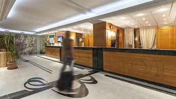 Zona de recepción de un hotel con suelo de mármol, mostrador de madera y una pantalla de televisión.