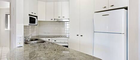 A kitchen with white cabinets, a granite countertop, stainless steel appliances, and a tiled backsplash.