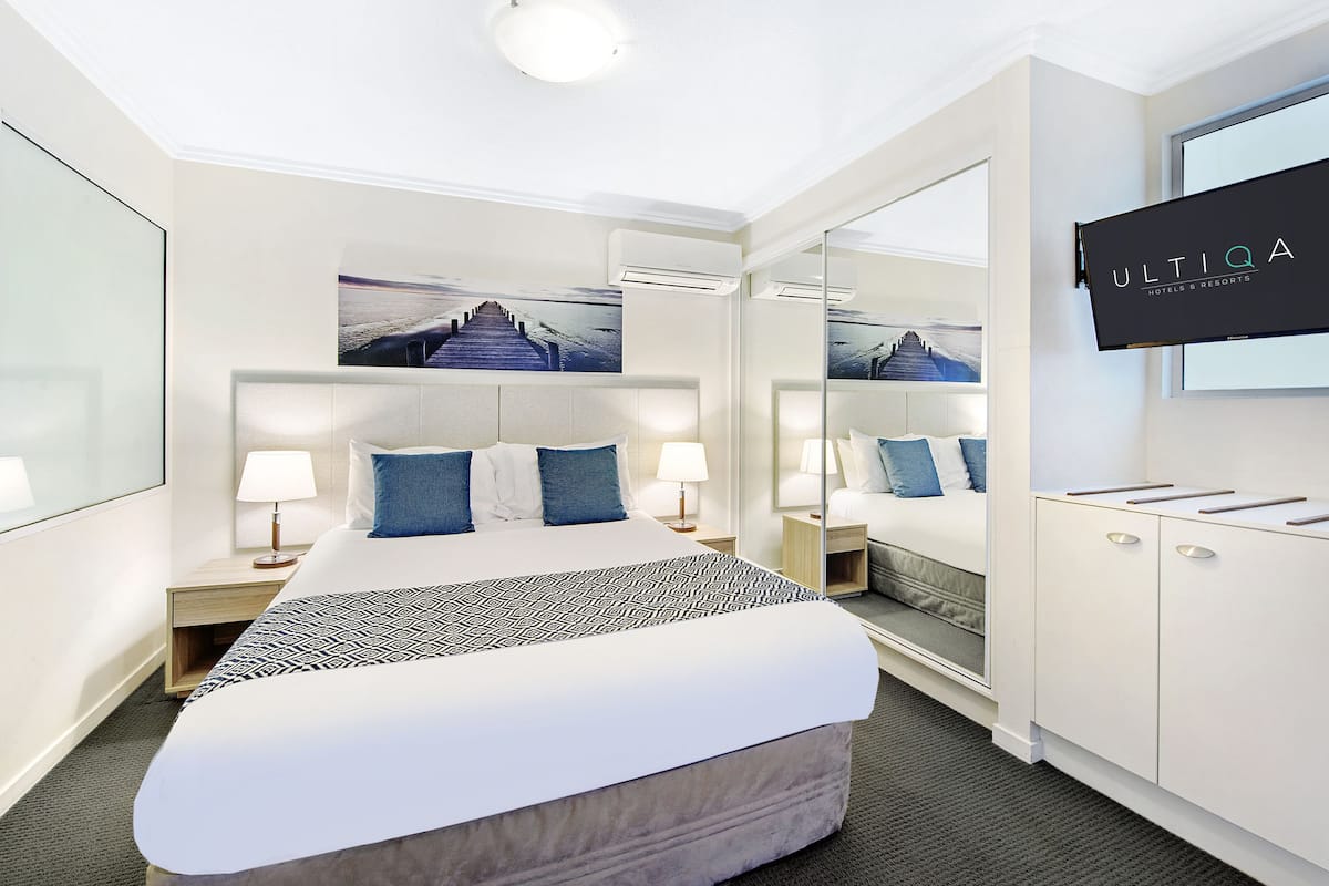 A hotel room with a large bed, a bedside table with a lamp, a mirror, and a television on the wall.