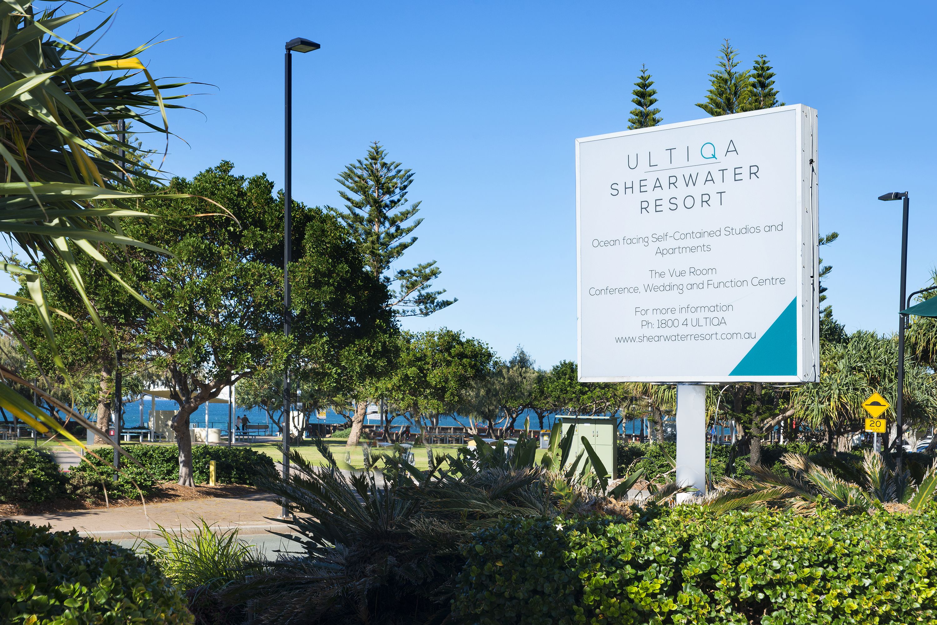Een bordje voor SULTIQA SHEARWATER RESORT met een lijst van voorzieningen, waaronder studio's en appartementen met uitzicht op de oceaan, The Vue Room, en een congres-, trouw- en evenementenlocatie.