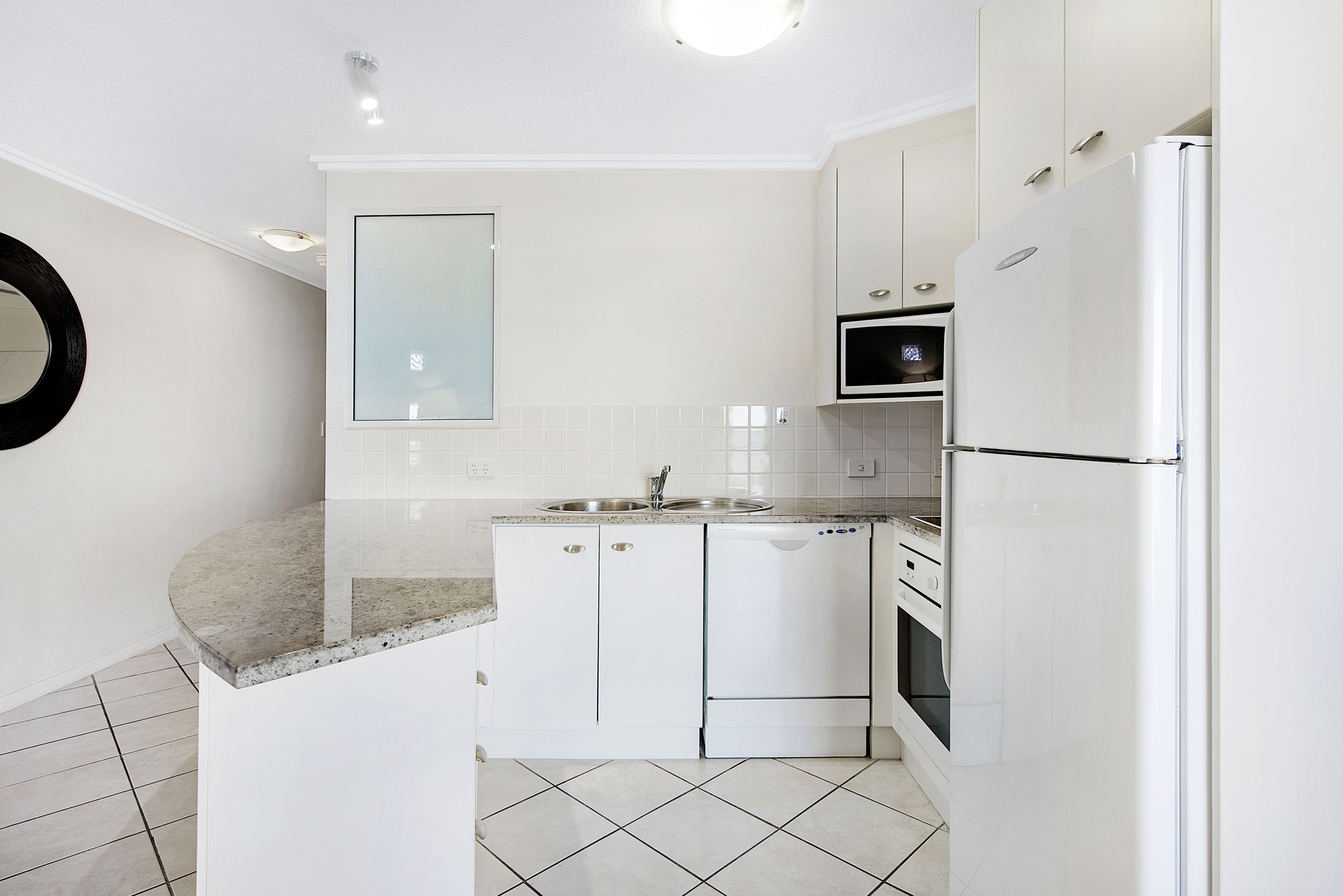 Une cuisine moderne avec des meubles blancs, un plan de travail en granit, un four encastré et un réfrigérateur.