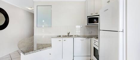 Une cuisine moderne avec des meubles blancs, un plan de travail en granit, un four encastré et un réfrigérateur.