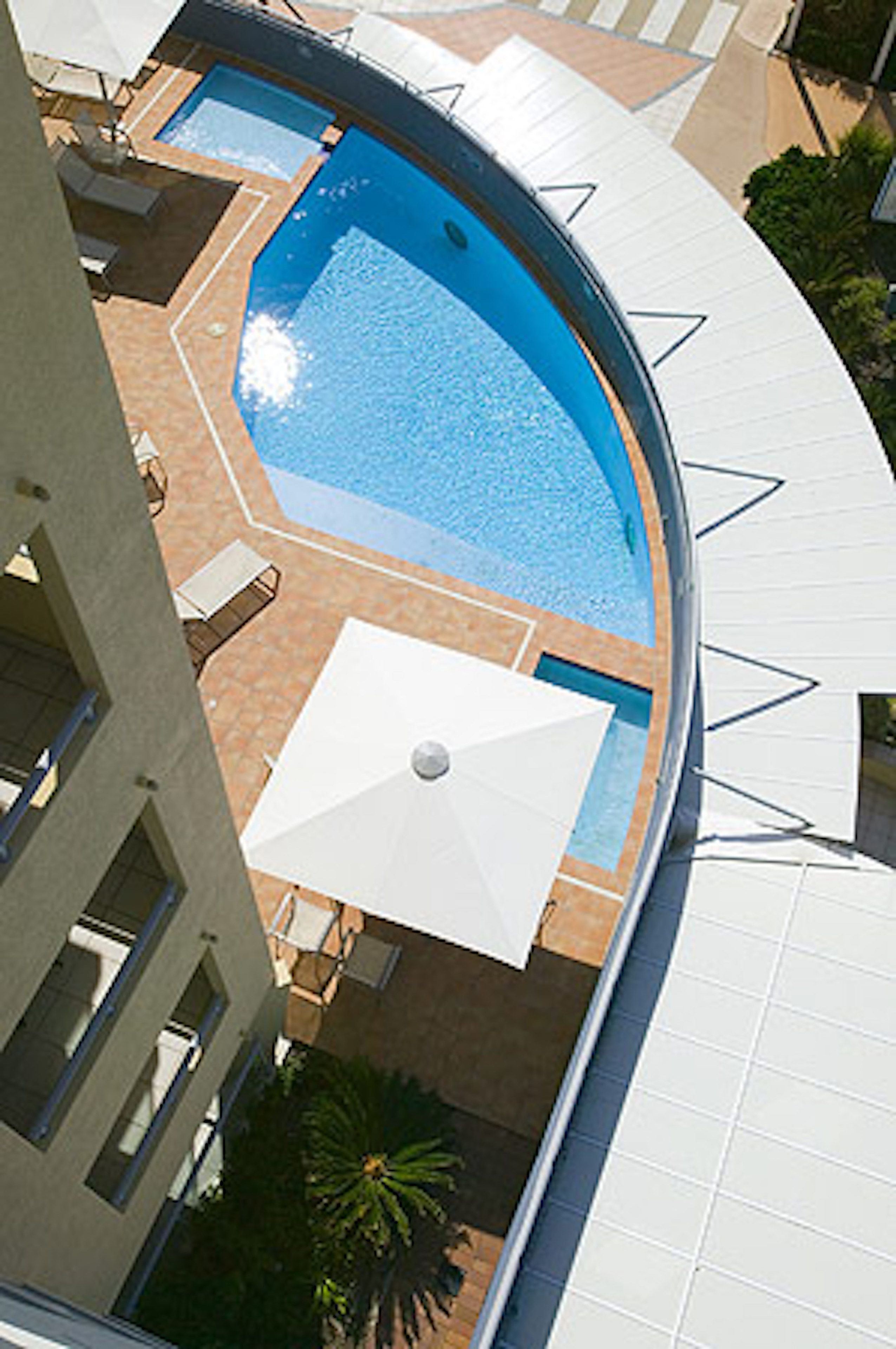 A rooftop pool with a curved edge, surrounded by lounge chairs and umbrellas.