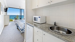 A modern kitchen with a built-in microwave, a stainless steel sink, and a view of the ocean through large windows.