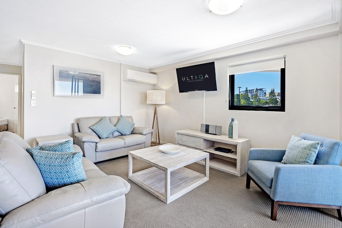 A modern living room with a sofa, armchair, coffee table, TV, and artwork.