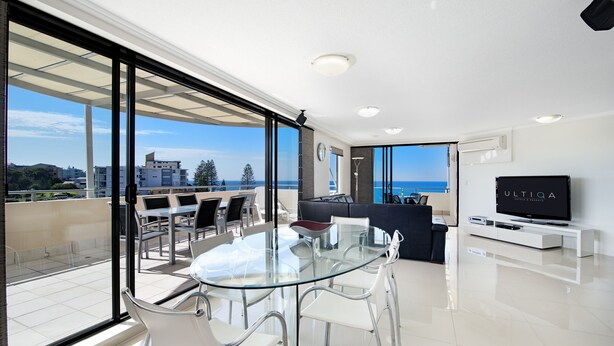 A modern living room with a glass table, white chairs, a sofa, and a TV on a white stand.