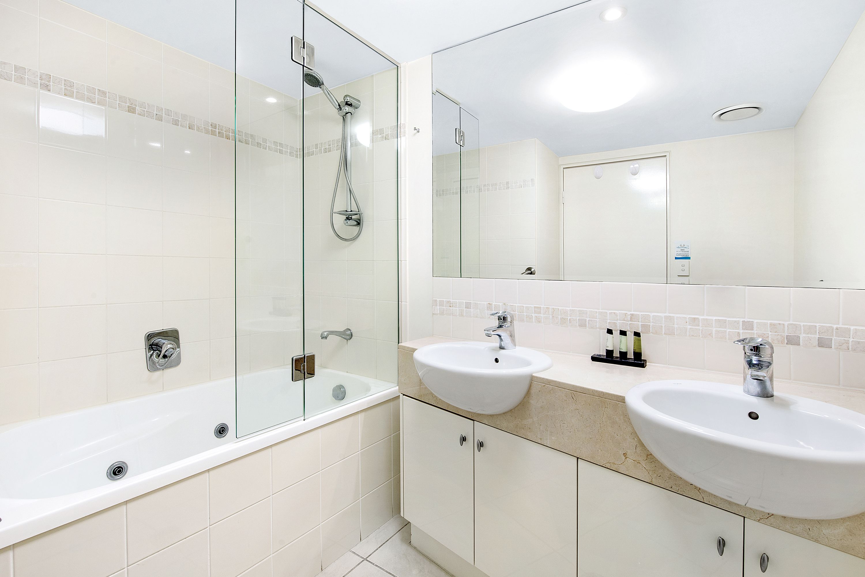 A modern bathroom with a glass-enclosed shower, a freestanding bathtub, and two sinks with a mirror above.