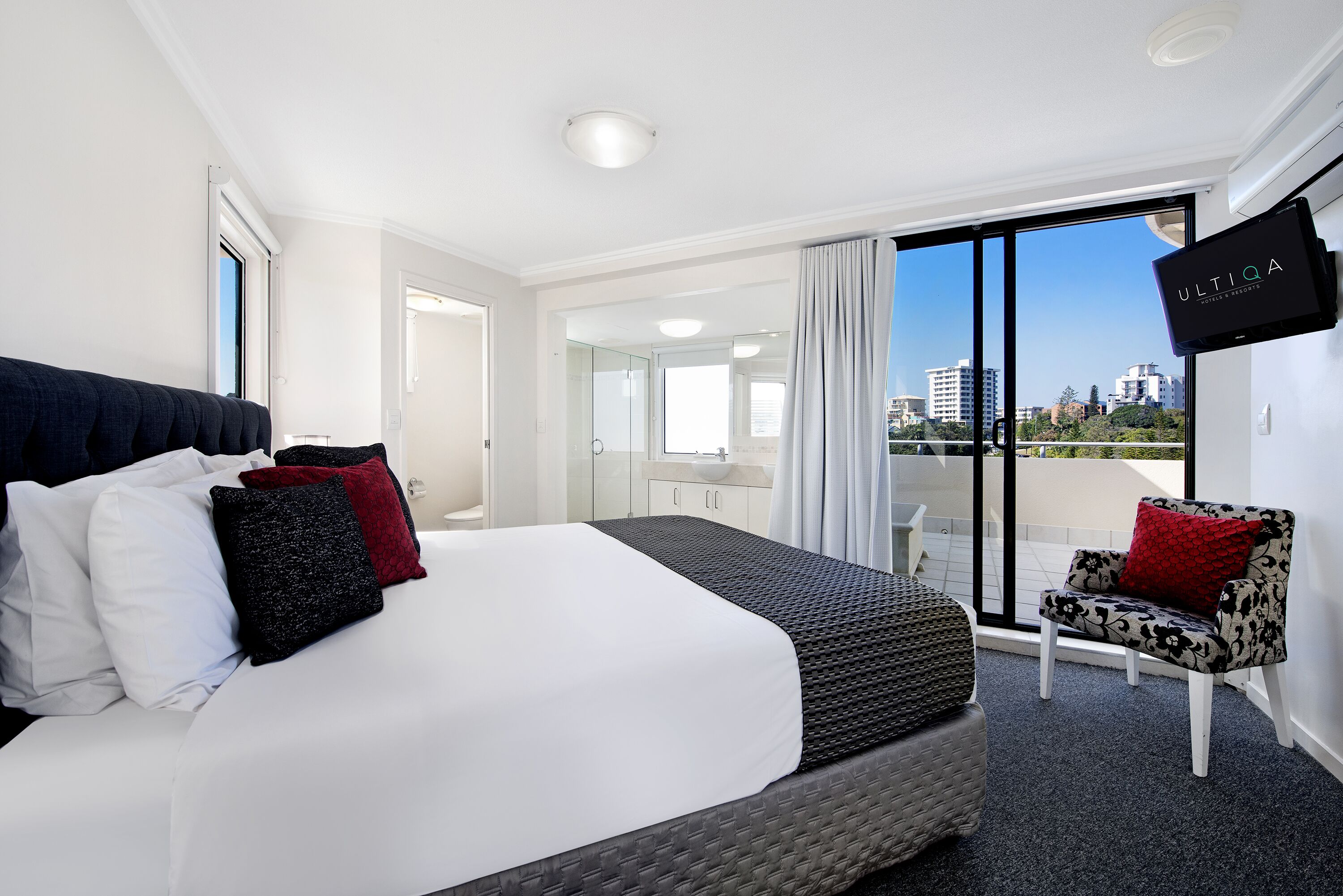 Une chambre d’hôtel avec un grand lit, une télévision et un balcon offrant une vue sur la ville.