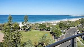 A coastal view with a beach, greenery, and a road with marked lanes.