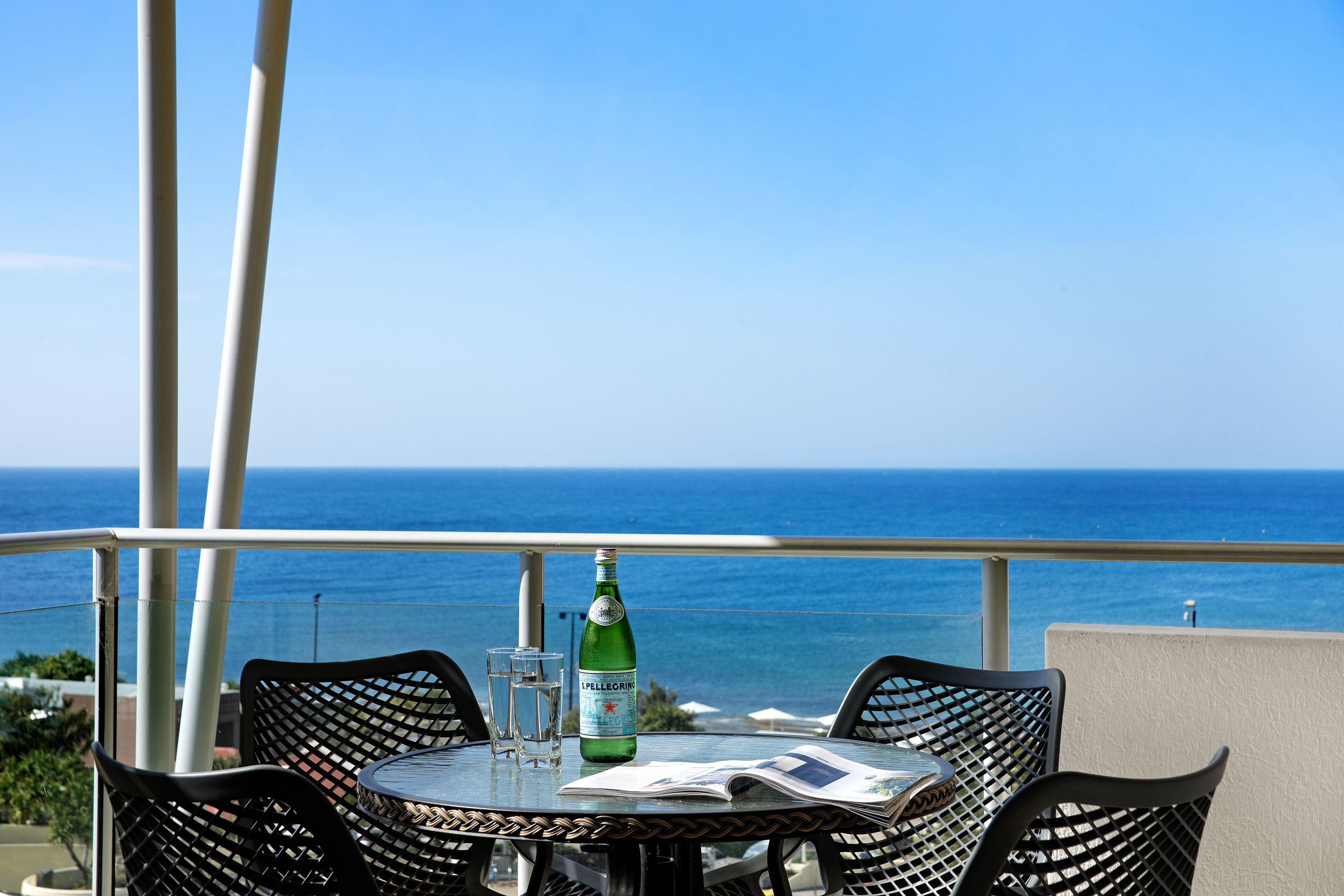 Une table ronde avec une bouteille d’eau Pellegrino, deux verres et un menu, le tout placé sur un balcon donnant sur l’océan.