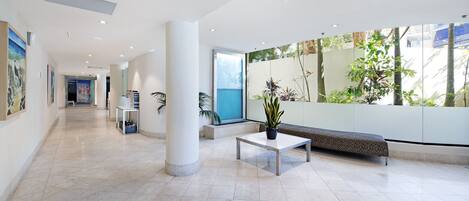 A modern lobby with a tiled floor, a bench, a table with a plant, and a large window with a view of greenery.