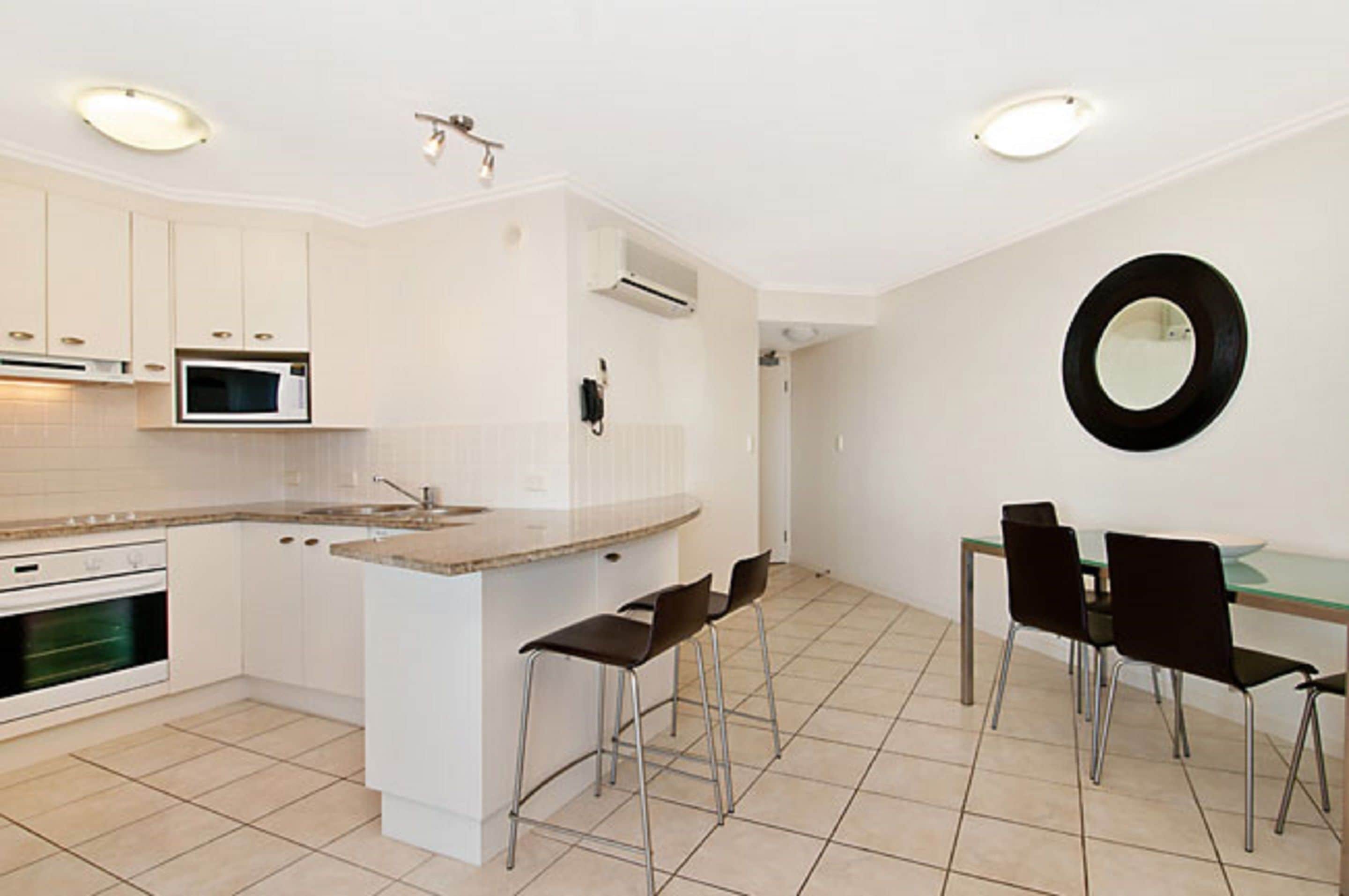 A modern kitchen with white cabinets, a microwave, and a dining area with a glass table and black chairs.