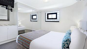 A modern hotel room with a large bed, a bedside table with a lamp, a wardrobe, a mirror, and a TV mounted on the wall.