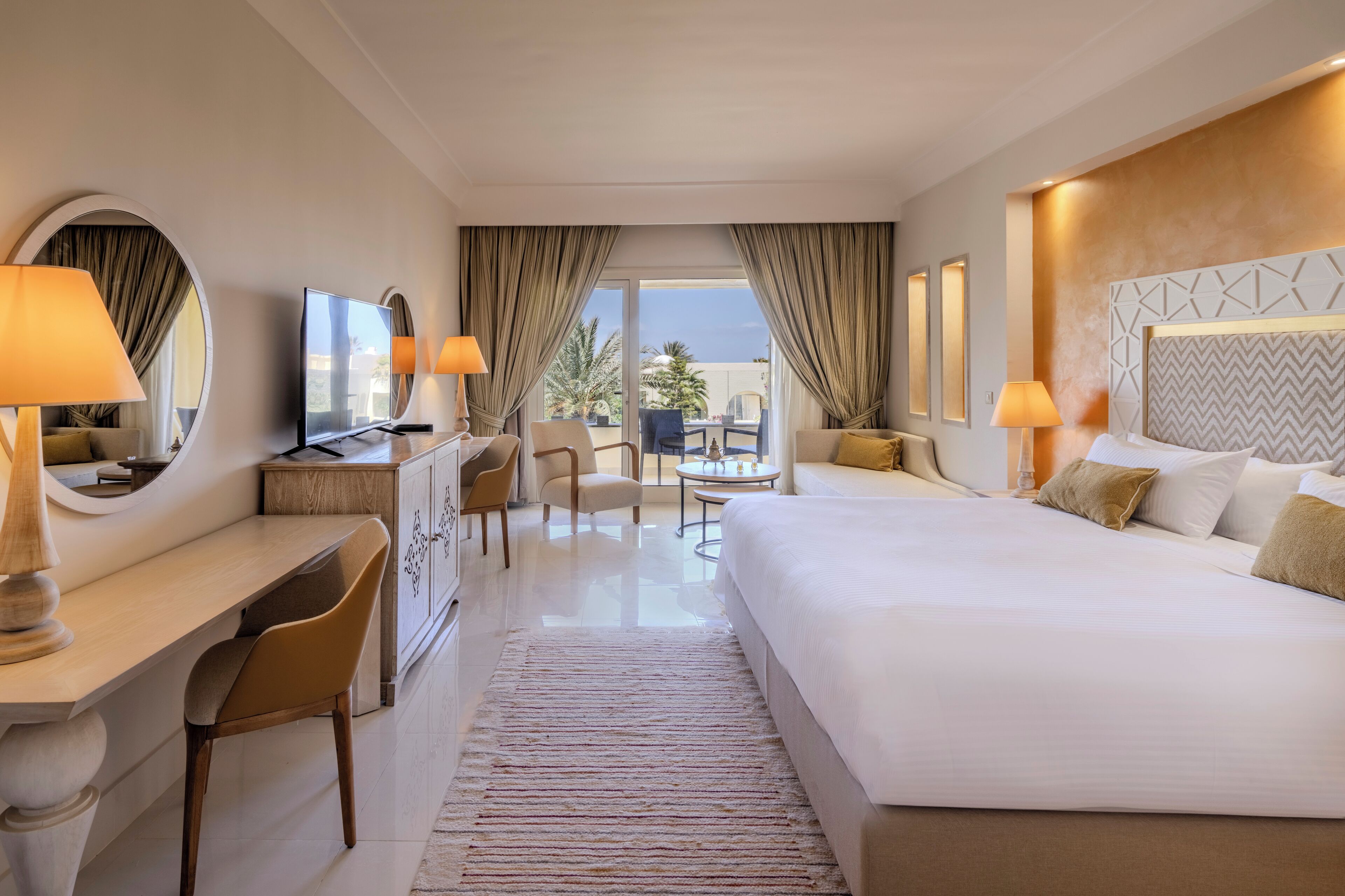 Une chambre d’hôtel avec un grand lit, un bureau avec une chaise, une petite table et une vue sur l’extérieur.