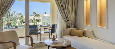 A modern living room with a sofa, two armchairs, a small round table, and a balcony with a view of palm trees and buildings.
