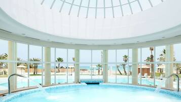 Ein großer, überdachter Swimmingpool mit freiem Blick auf den Strand und Palmen durch große Fenster.