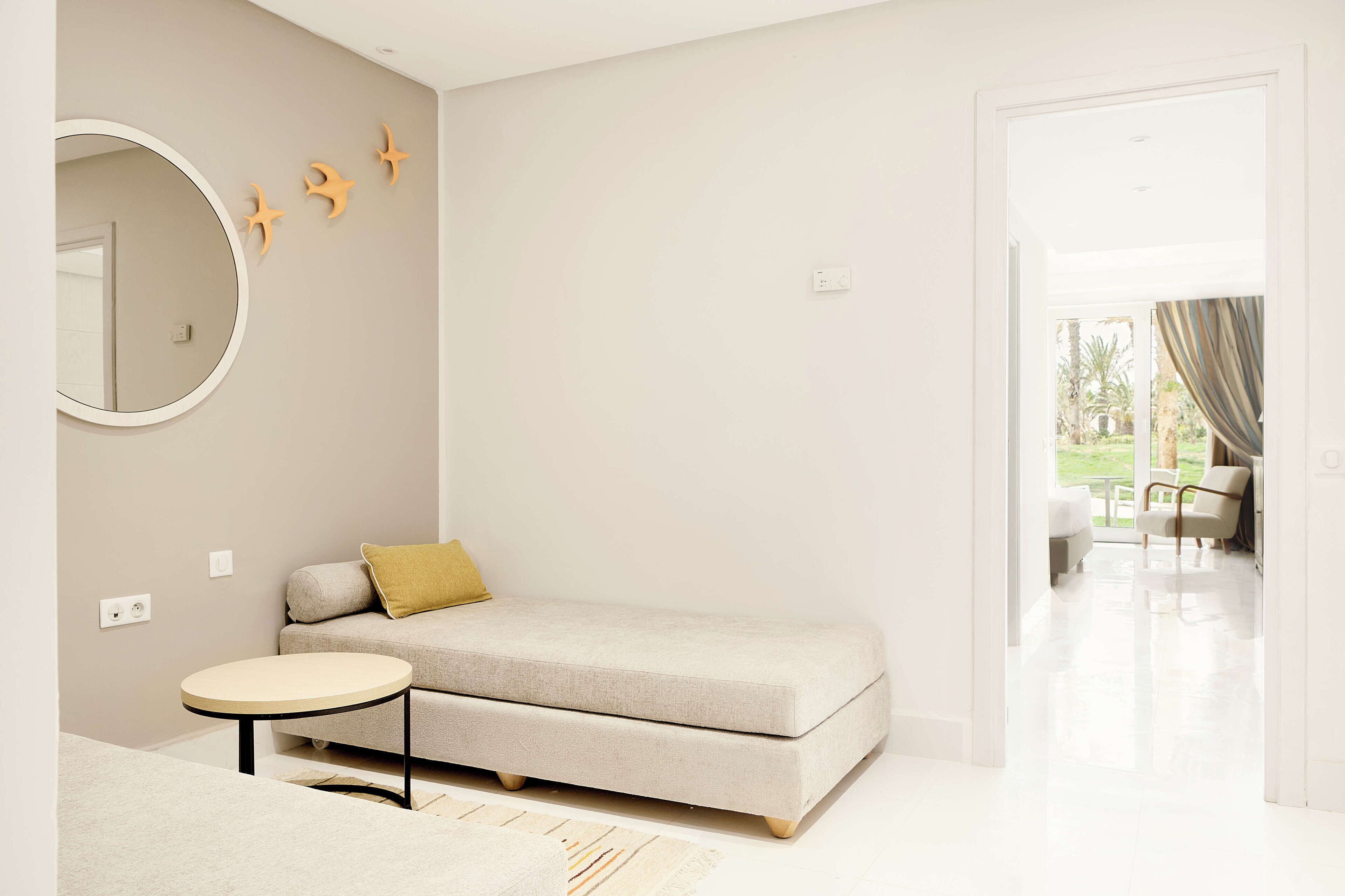 Un dormitorio moderno con un sofá, un espejo redondo y una mesita.